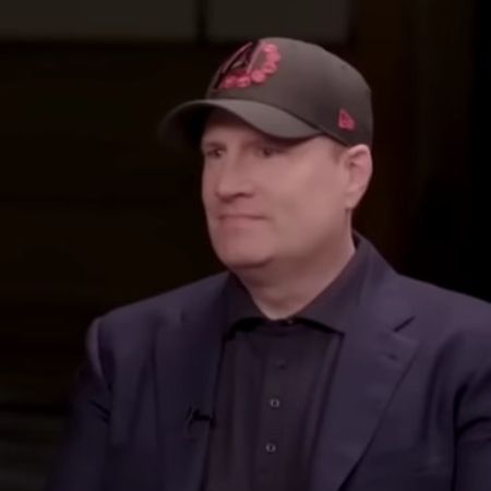 Kevin Feige is wearing a black suit and a baseball cap.